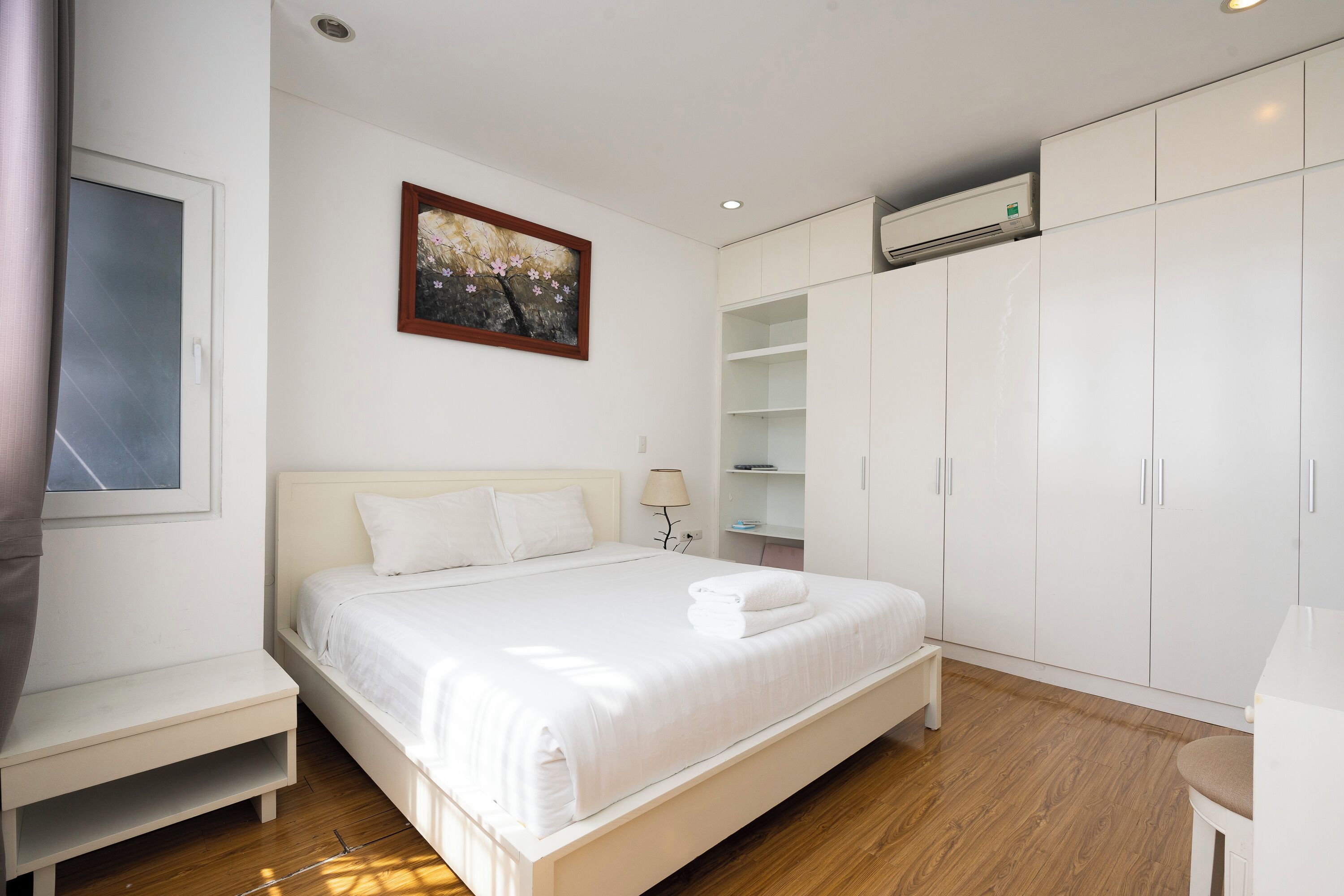 Een slaapkamer met een bed, nachtkastje, garderobe en een schilderij aan de muur.