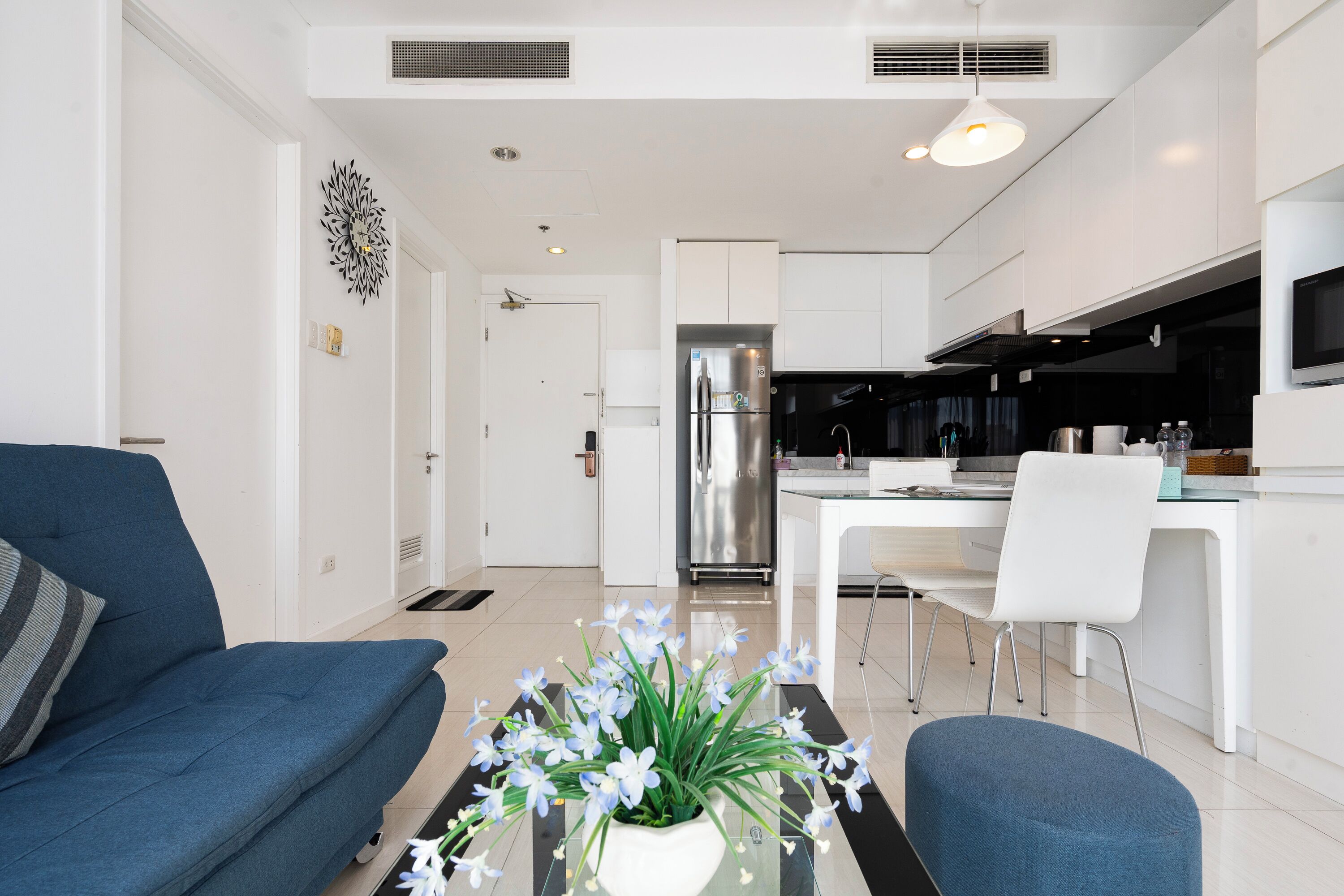 A modern living room with a sofa, a dining table, and a kitchen area with a refrigerator and microwave.