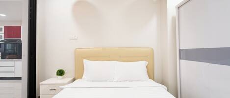 A neatly made bed with white bedding, a small bedside table with a plant, and a modern pendant light.