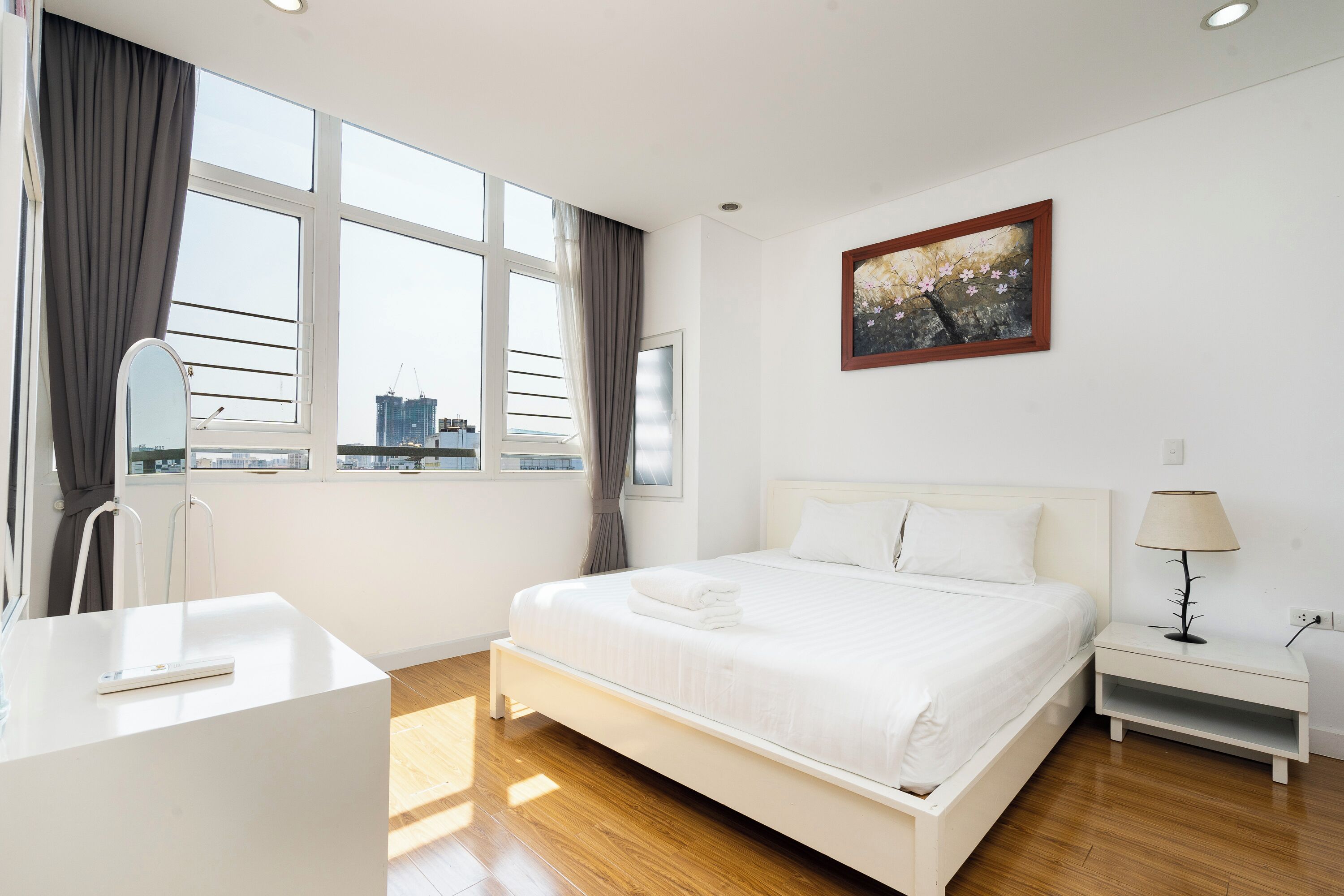 Habitación de hotel moderna con una cama grande, una mesita de noche con lámpara, una ventana con cortinas y vistas a la ciudad.