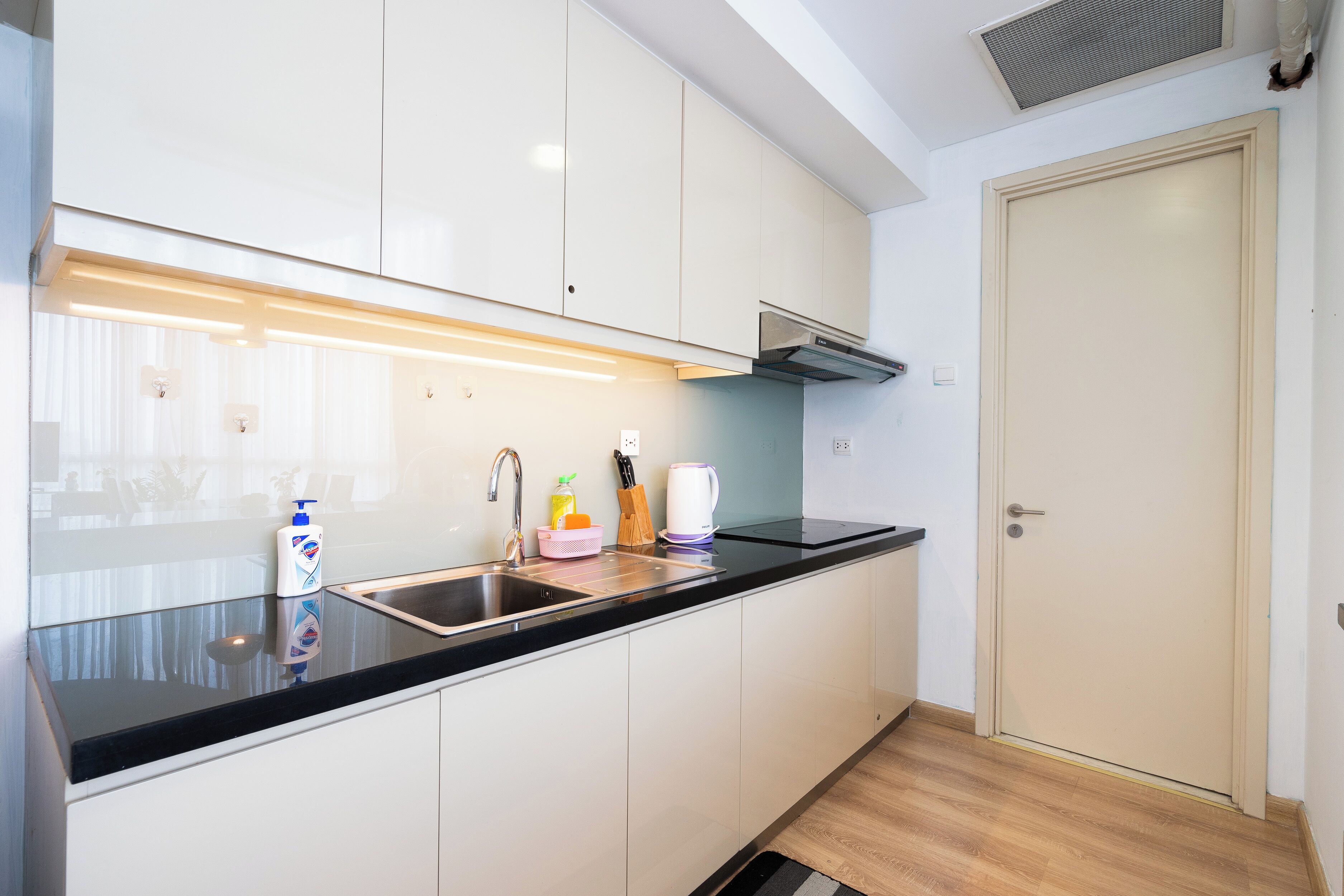 A modern kitchen with a black countertop, white cabinets, a stainless steel sink, and a built-in range hood.