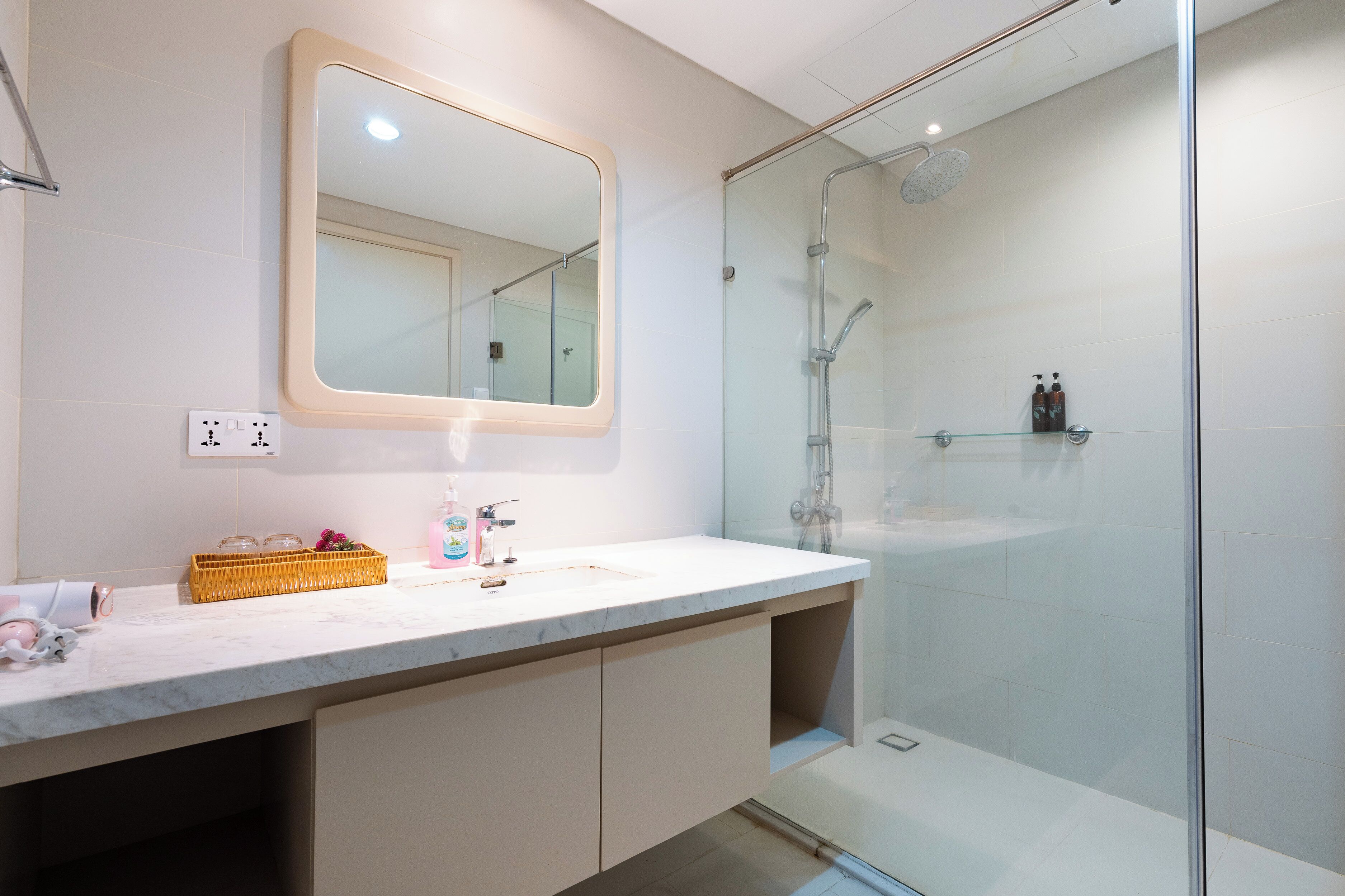 Een moderne badkamer met een douchecabine van glas, een marmeren wastafel en een spiegel boven het aanrecht.