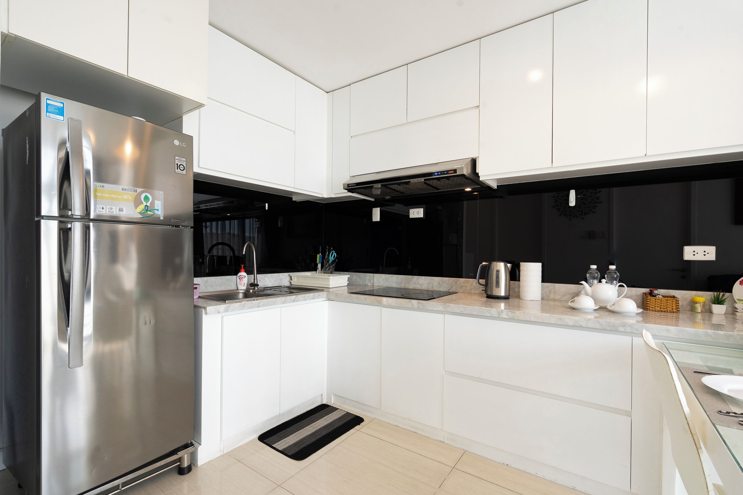 A modern kitchen with white cabinets, a stainless steel refrigerator, and a black backsplash.