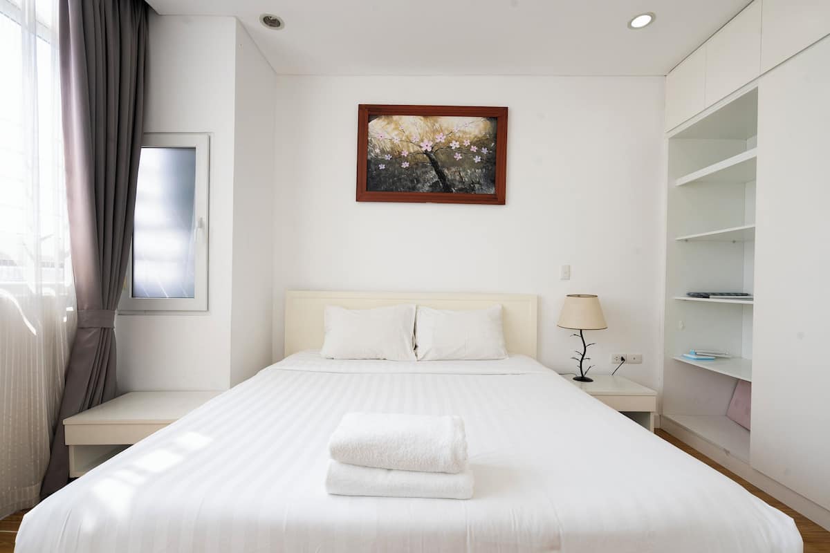 A hotel room with a bed, a nightstand, a lamp, a painting, and a wardrobe.