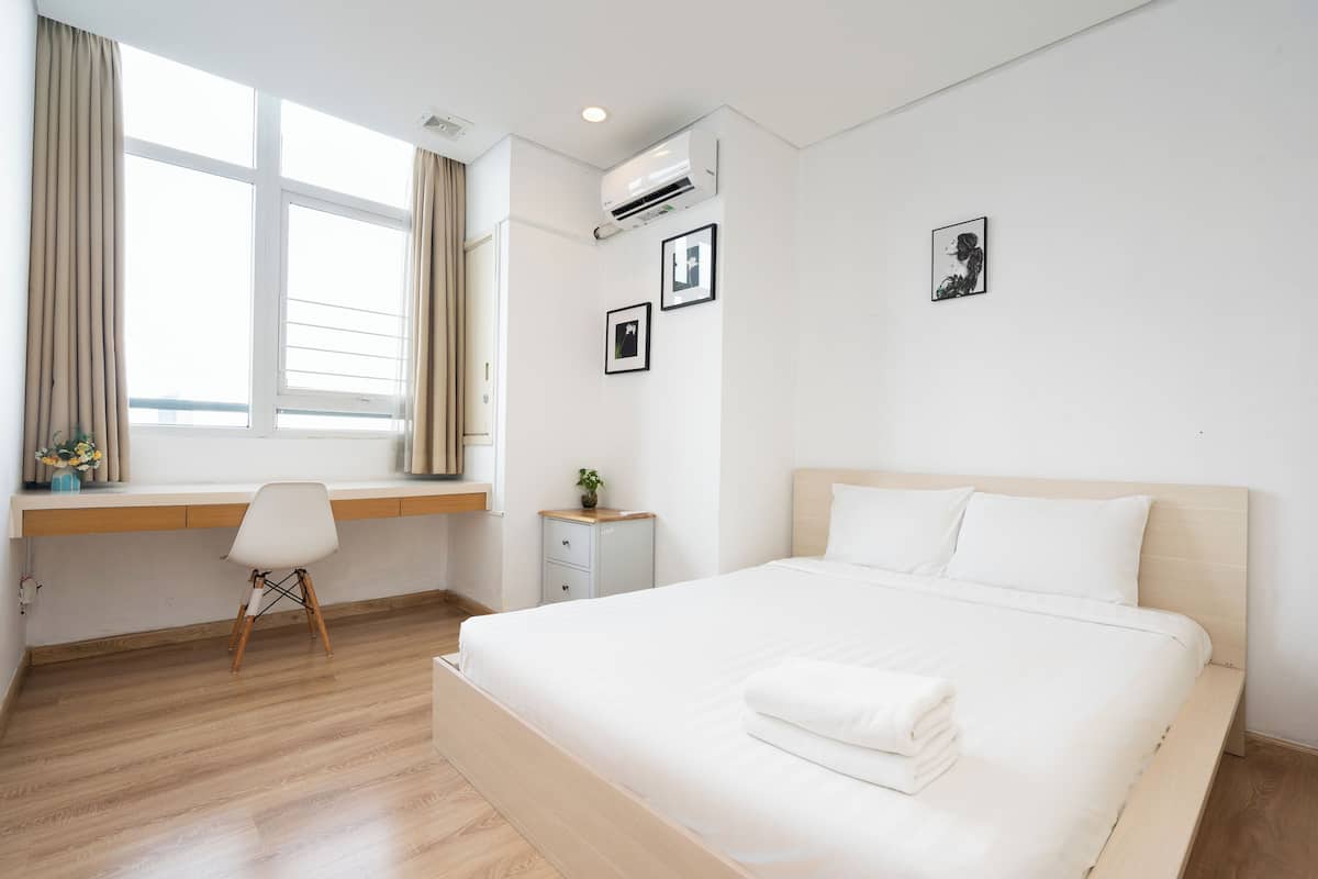 A modern hotel room with a large bed, a desk, and a window with curtains.