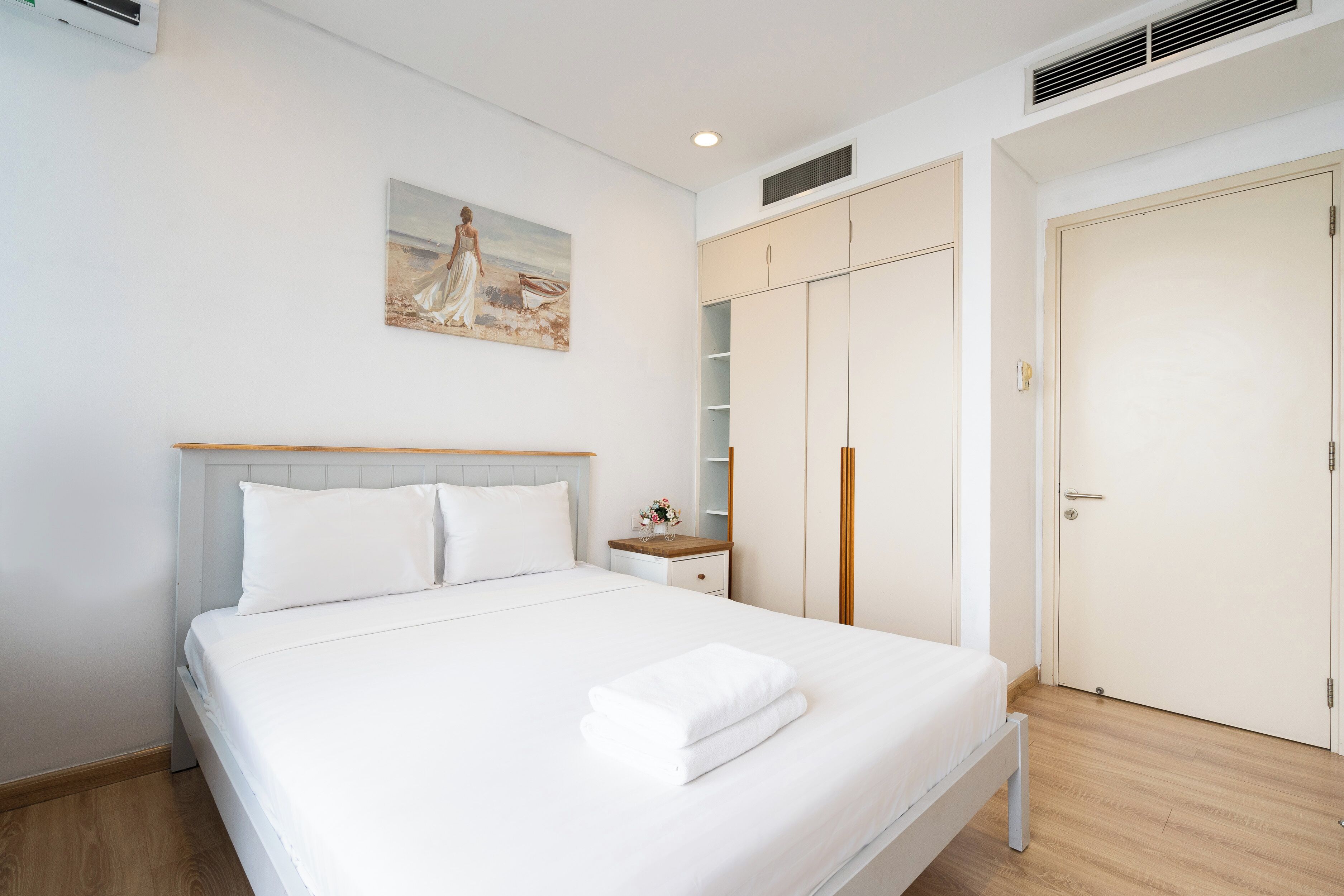 Een slaapkamer met een bed, nachtkastje, schilderij, kast en een deur.
