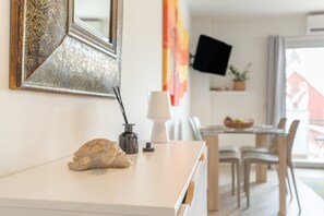 Ein modernes Zimmer mit einer weißen Kommode, einer dekorativen Schildkrötenfigur, einem an der Wand montierten Fernseher und einem Essbereich mit Stühlen und einem Tisch.