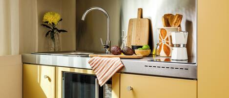 A kitchen with a stainless steel sink, wooden cutting board, and a fruit bowl.
