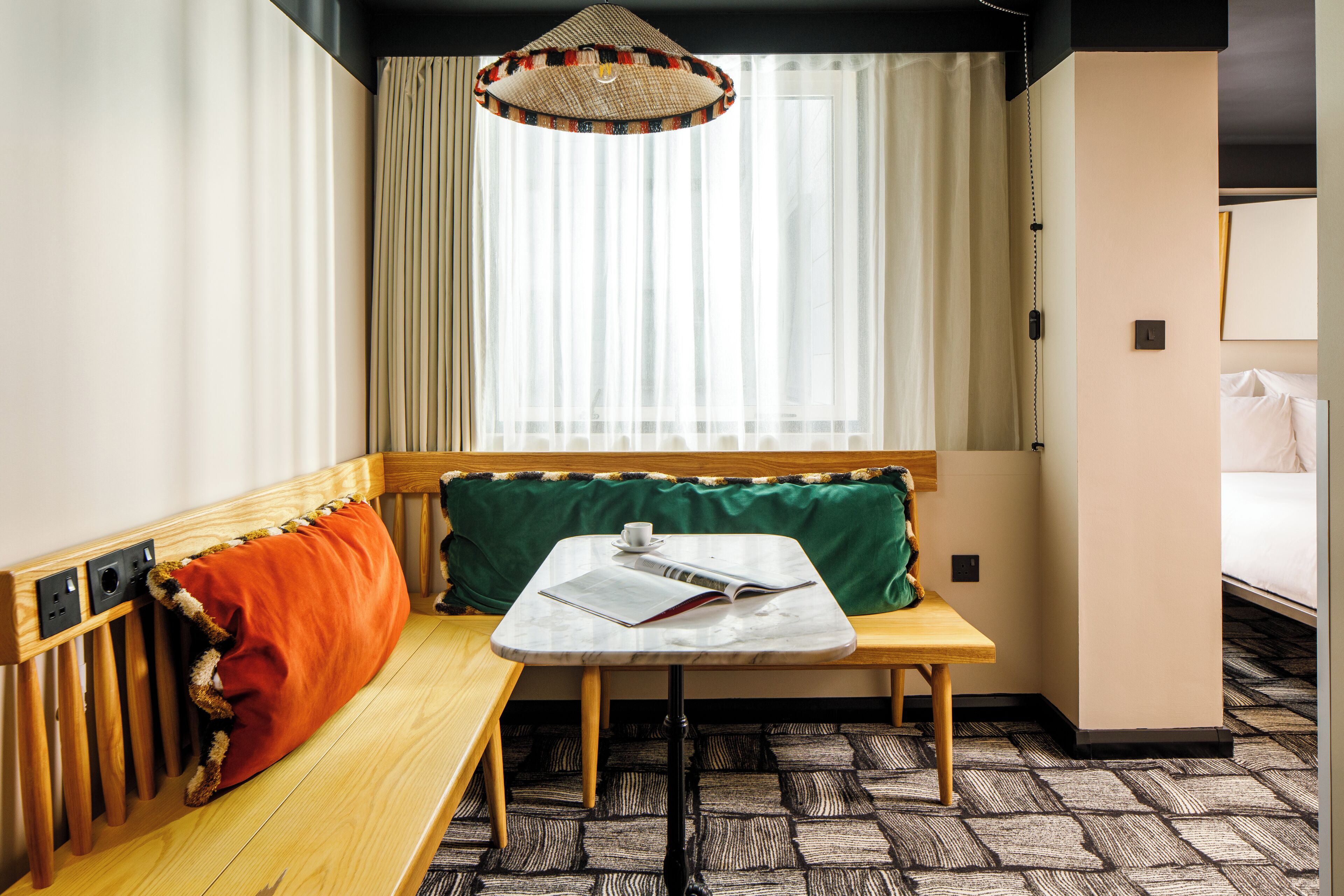 Een kleine kamer met een bank, een tafel met een boek, een raam met gordijnen en een hanglamp.