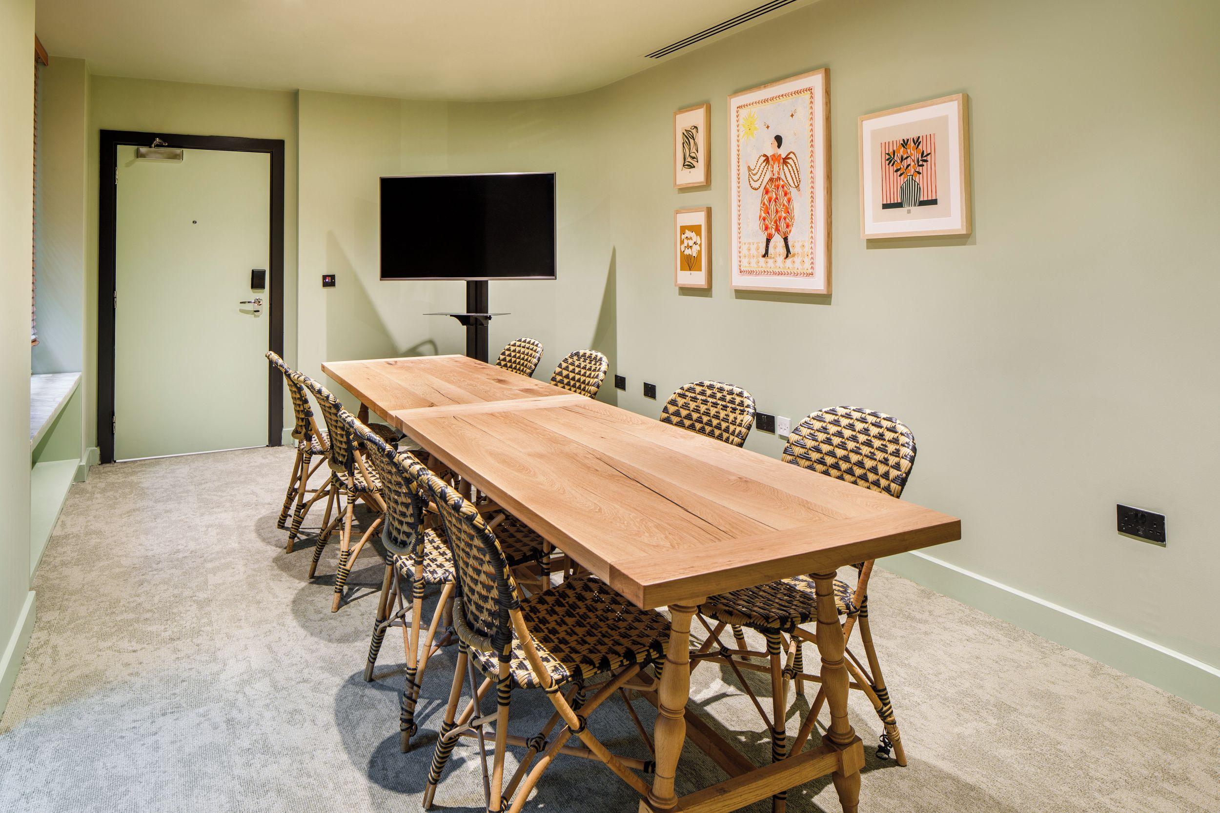 A conference room with a long table, wicker chairs, a flat-screen TV, and framed artwork on the walls.
