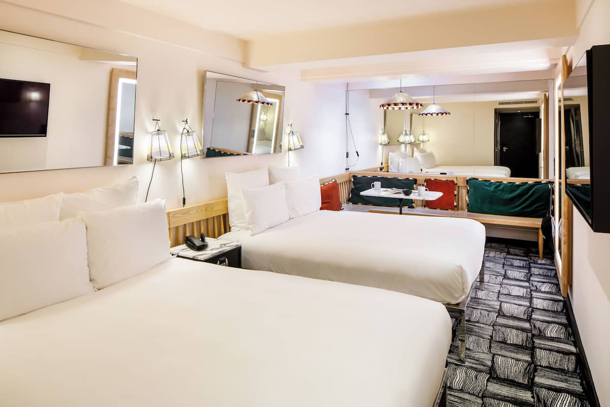 A hotel room with two beds, a desk, a chair, a mirror, and a television.