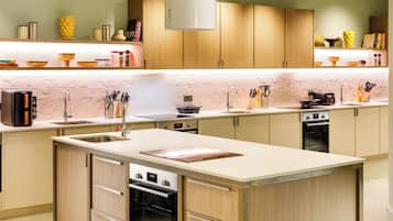 A modern kitchen with wooden cabinets, a central island, a built-in oven, and a coffee maker.