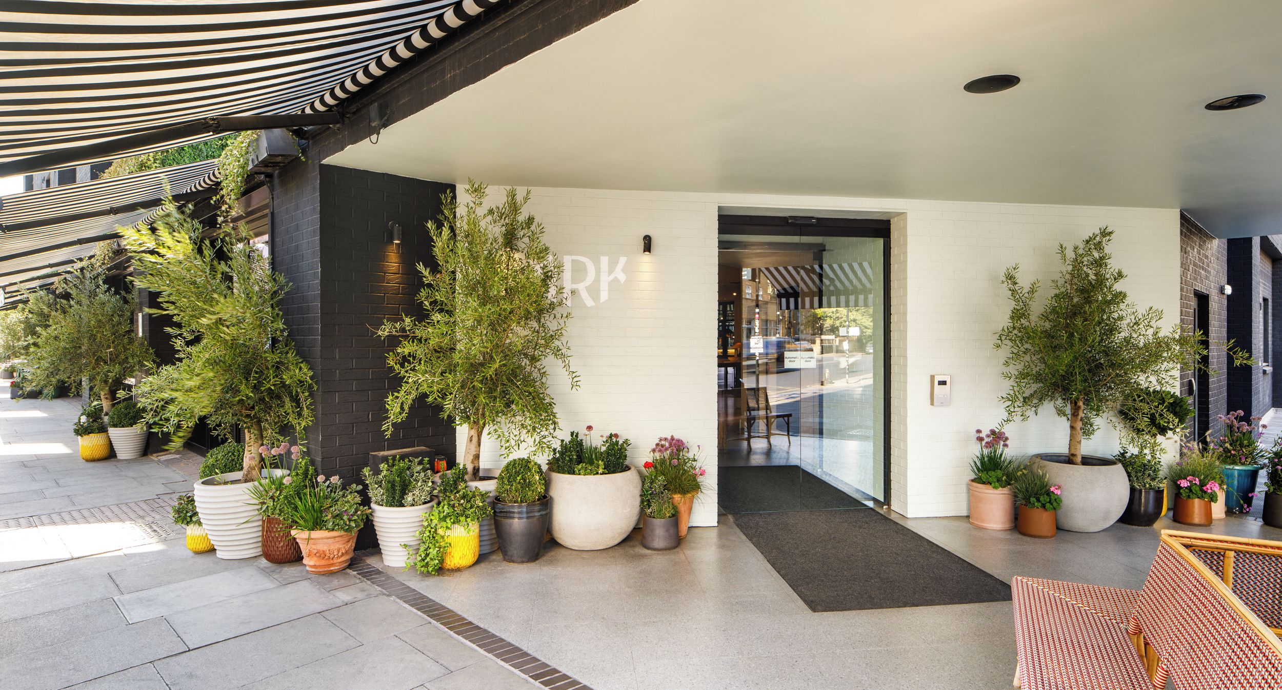 A hotel entrance with a covered walkway, potted plants, and a modern interior.
