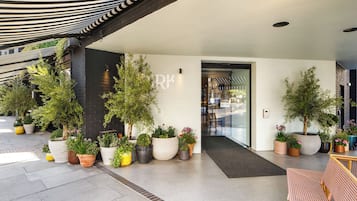 A hotel entrance with a covered walkway, potted plants, and a modern interior.