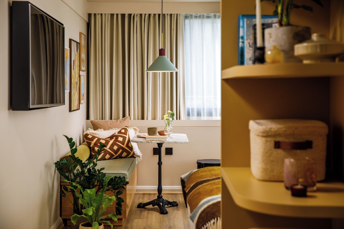 A cozy living room with a sofa, a table, a floor lamp, and a bookshelf.