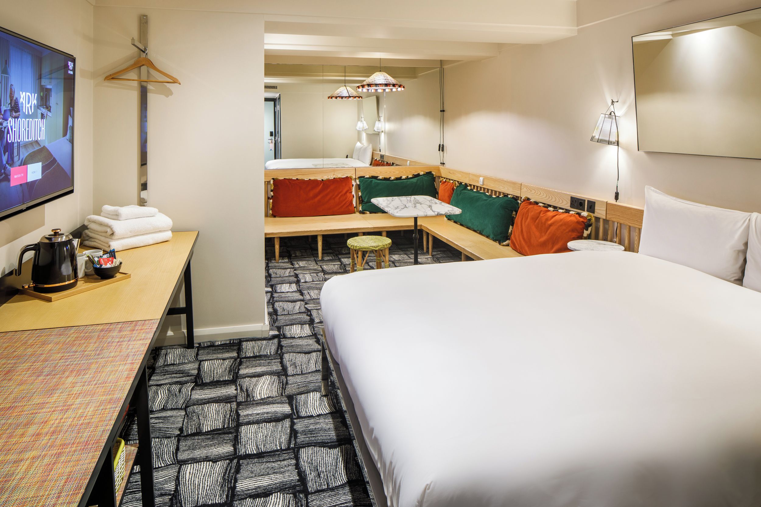 Ett hotellrum med en säng, ett skrivbord med en vattenkokare, en TV och en sittgrupp med ett bord och stolar.