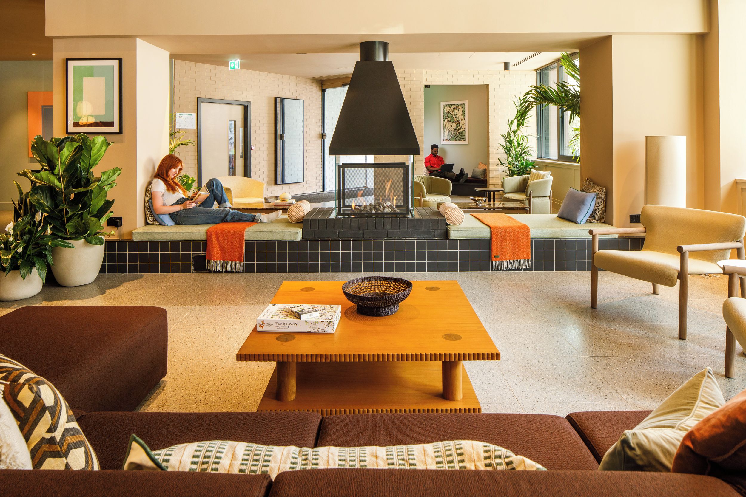 A modern lounge area with seating, a fireplace, and potted plants.