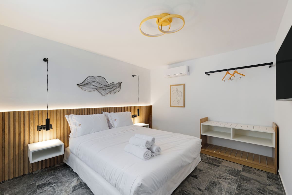Una habitación de hotel moderna con cama, mesitas de noche, repisa en la pared y lámpara de techo.