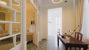 A hallway with a wooden dining table, chairs, a vase with branches, and a door leading to another room. - Kismet Urban Boutique (Heraklion)