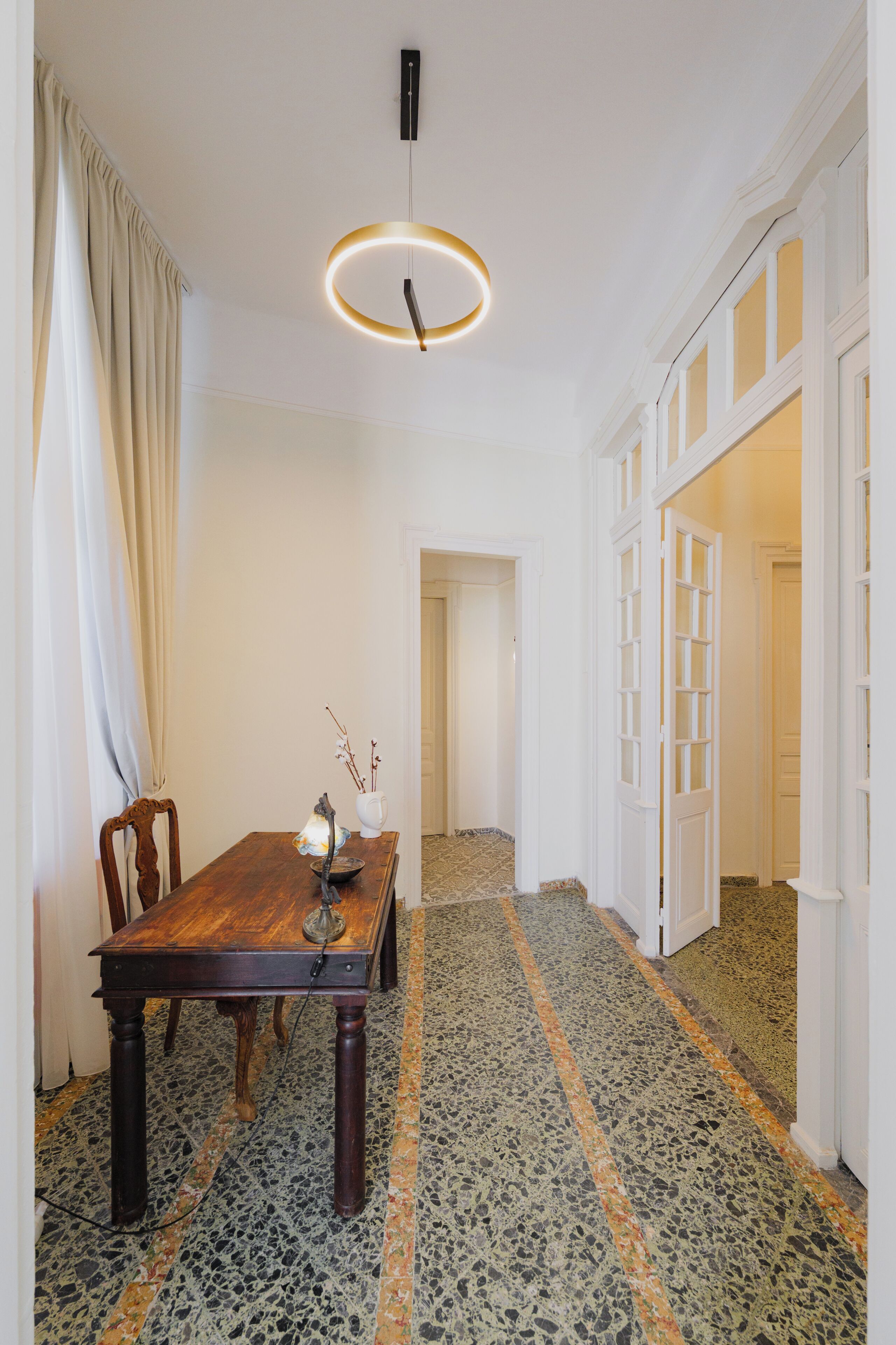 Un comedor con una mesa de madera, sillas, un florero con ramas y una lámpara colgante.