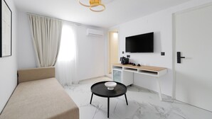 A modern hotel room with a bed, a small round table, a TV, a minibar, and a window with curtains. - Kismet Urban Boutique (Heraklion)