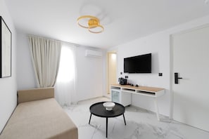 Une chambre d’hôtel moderne équipée d’un lit, d’une petite table ronde, d’une télévision, d’un minibar et d’une fenêtre avec des rideaux.