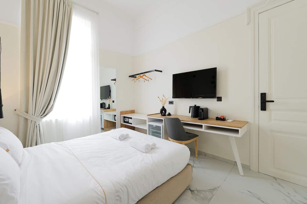 Habitación de hotel con cama, escritorio con silla, televisión y puerta.