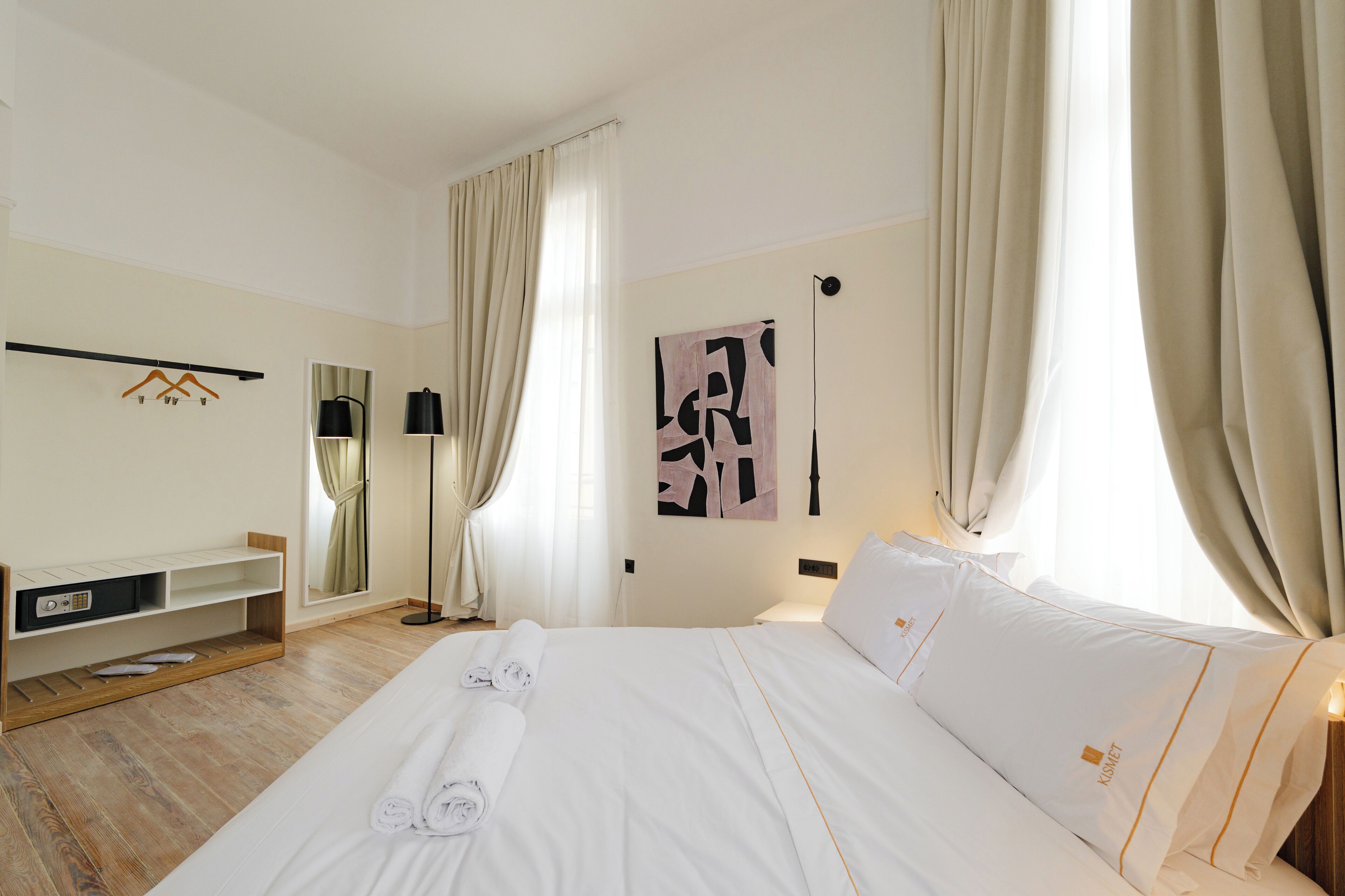 A hotel room with a neatly made bed, a mirror, a bedside table, and a wall-mounted artwork.