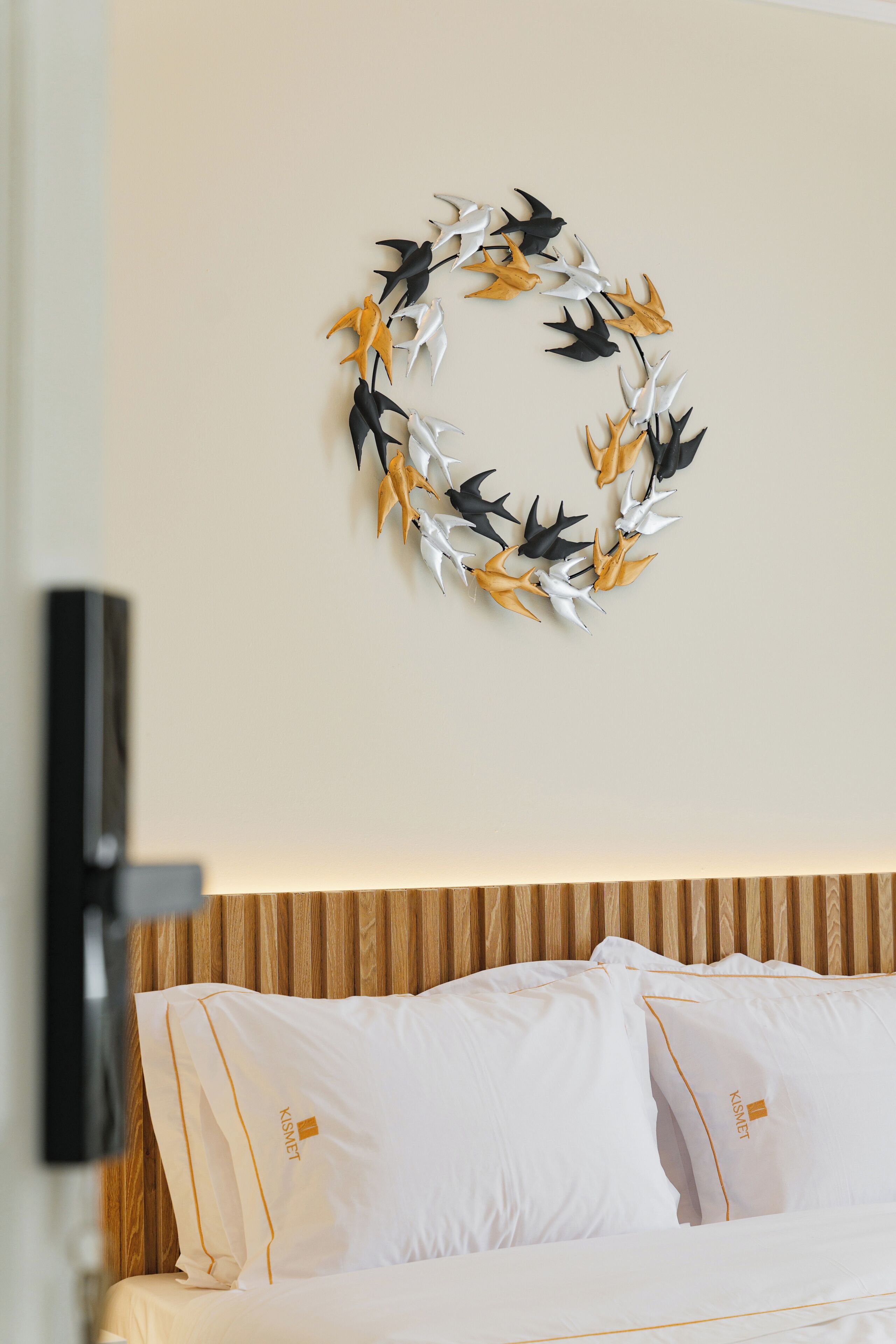 A hotel room with a bed, white bedding, a wooden headboard, and a wall-mounted decorative leaf wreath.