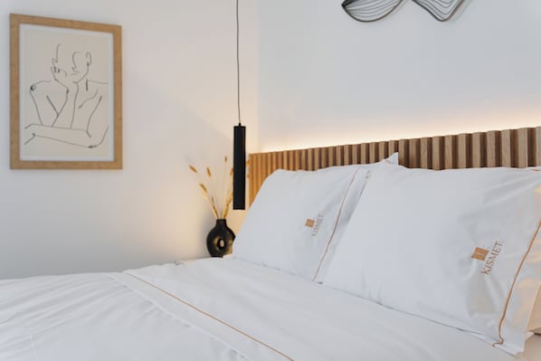 A neatly made bed with white linens and pillows, a framed artwork on the wall, and a bedside table with a vase.