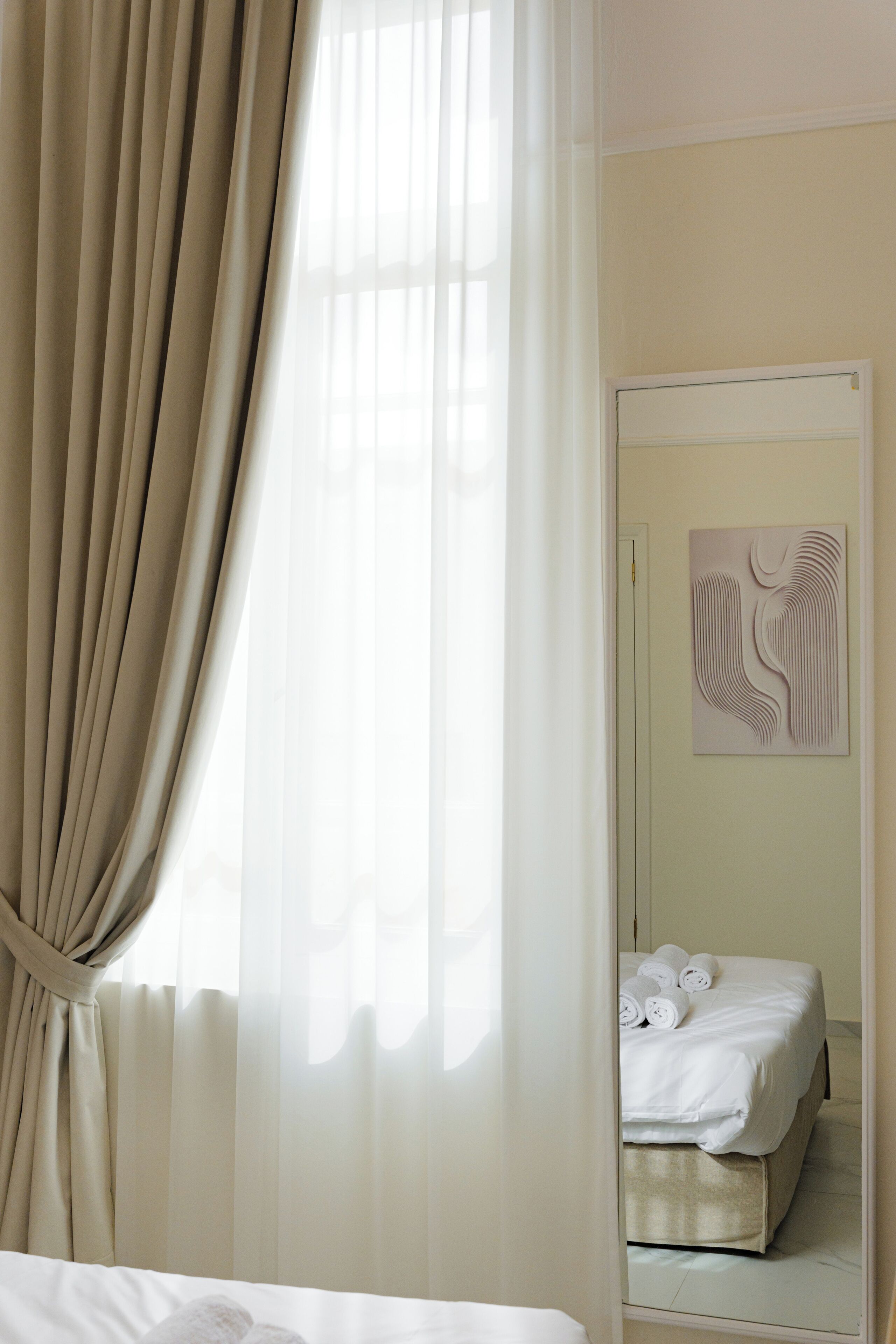 A hotel room with a bed, a mirror, and a wall art piece.