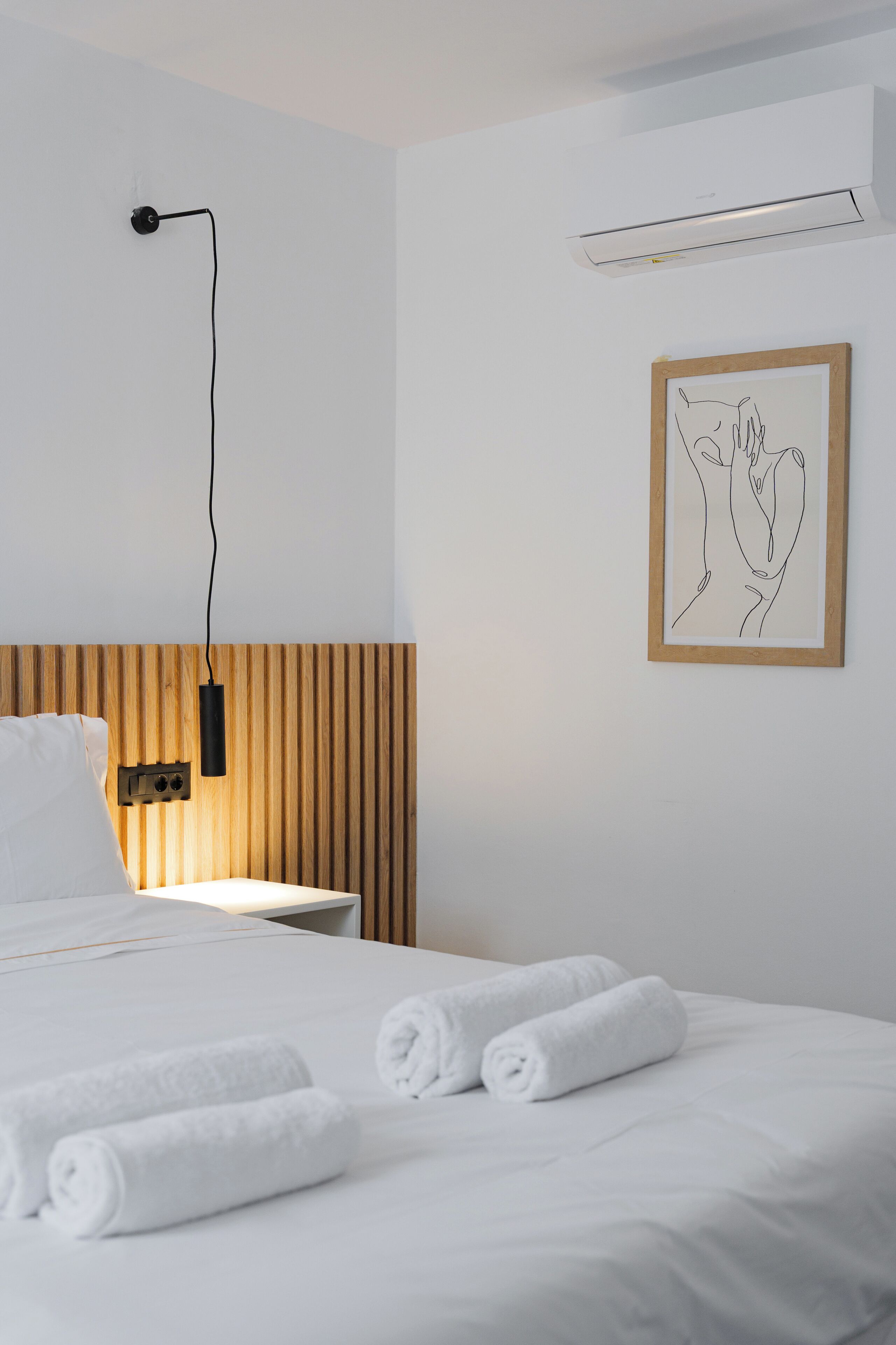 A hotel room with a bed, a nightstand, a wall-mounted air conditioner, and a framed picture.