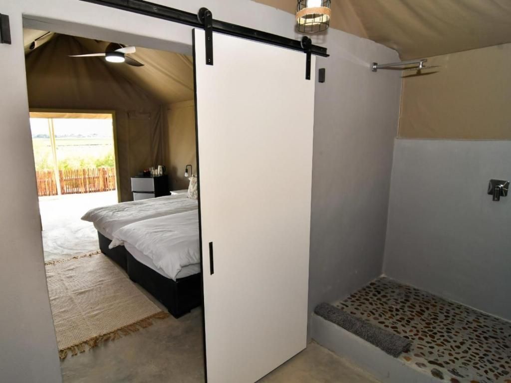 A tented room with a bed, a small table, and a shower area.