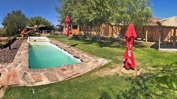 A swimming pool with stone edging, surrounded by a grassy lawn and trees.