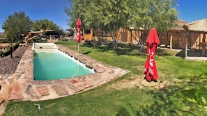 Una piscina con borde de piedra, rodeada de césped y árboles.