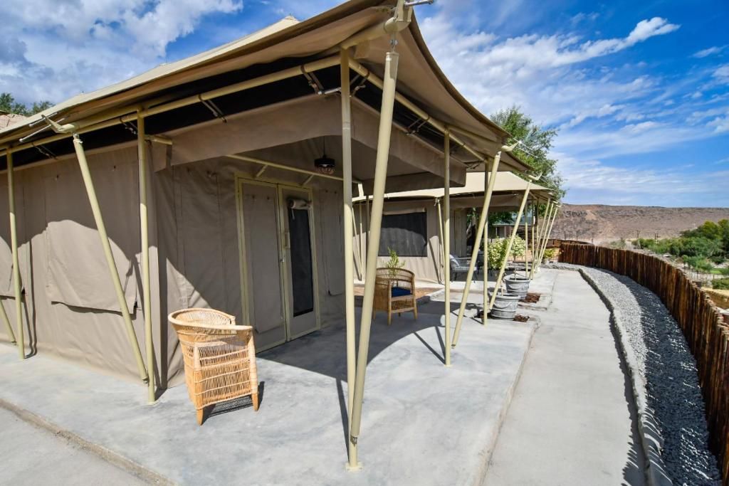 A tented accommodation with a concrete floor, a wicker chair, and a small table.
