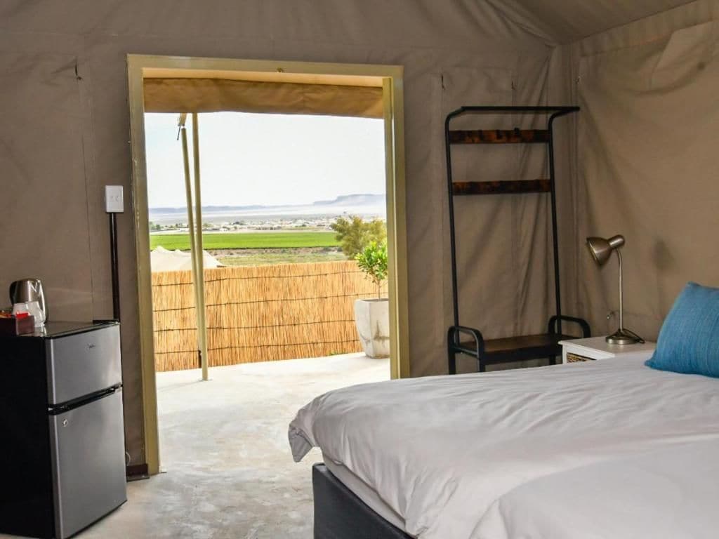 Un dormitorio con cama, escritorio, silla, lámpara y refrigerador.