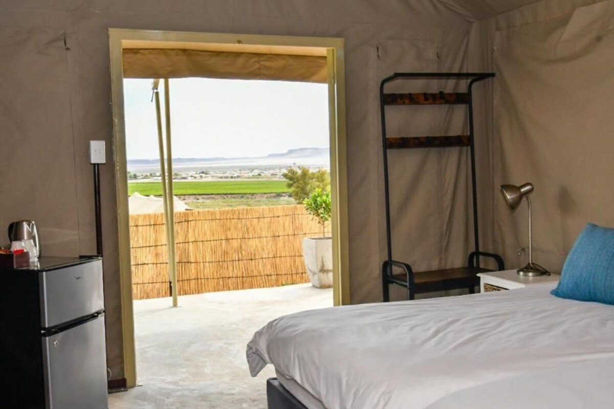 A bedroom with a bed, a desk, a chair, a lamp, and a view of the outdoors.