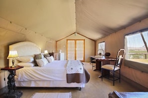 A tented room with a bed, desk, chair, and a view through a window. - Frontier River Resort (Vioolsdrif)