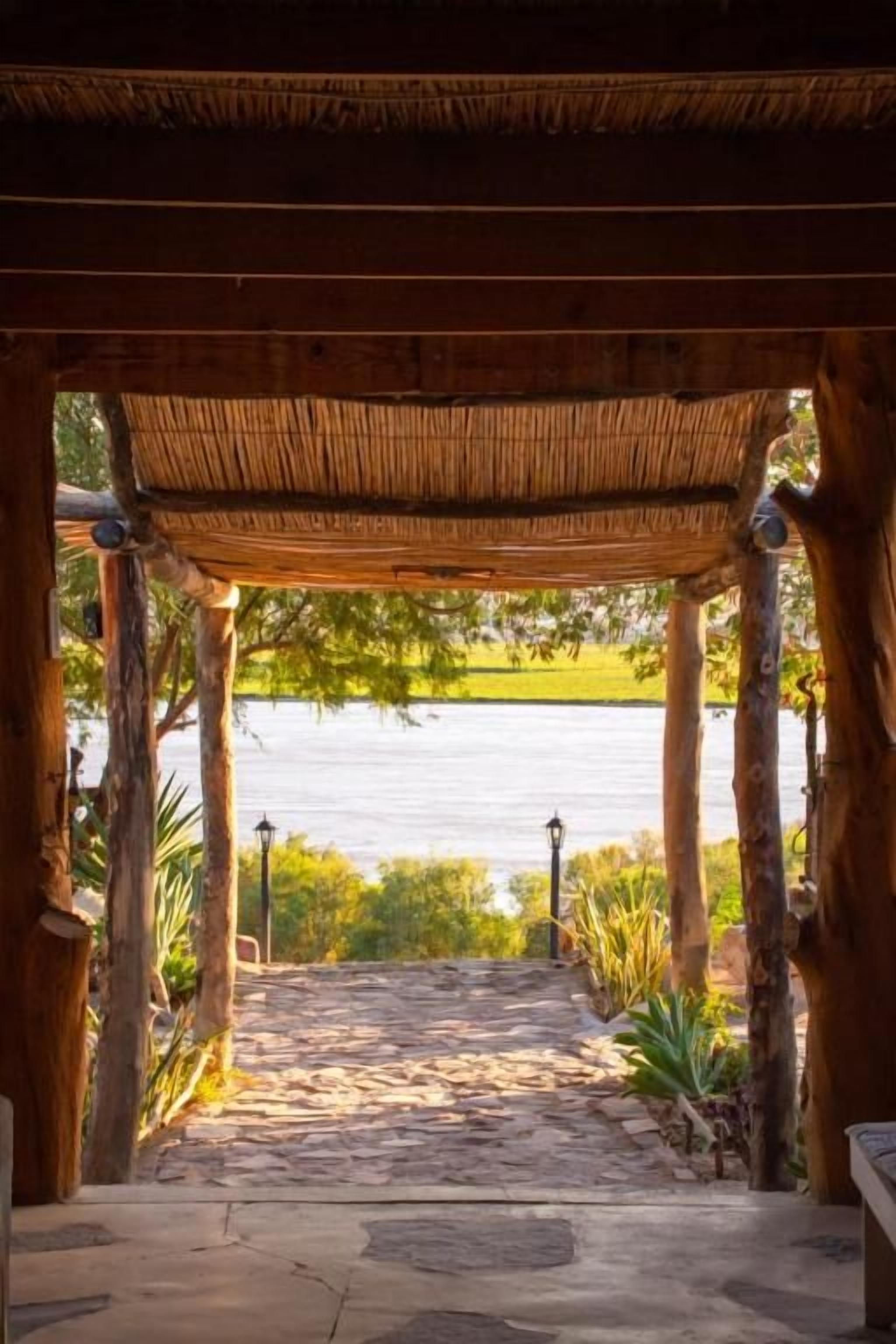 A wooden pergola structure with a stone pathway leading to a body of water.