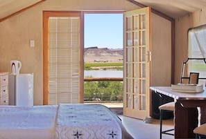 Un dormitorio con cama, escritorio y vista a un paisaje por una puerta.
