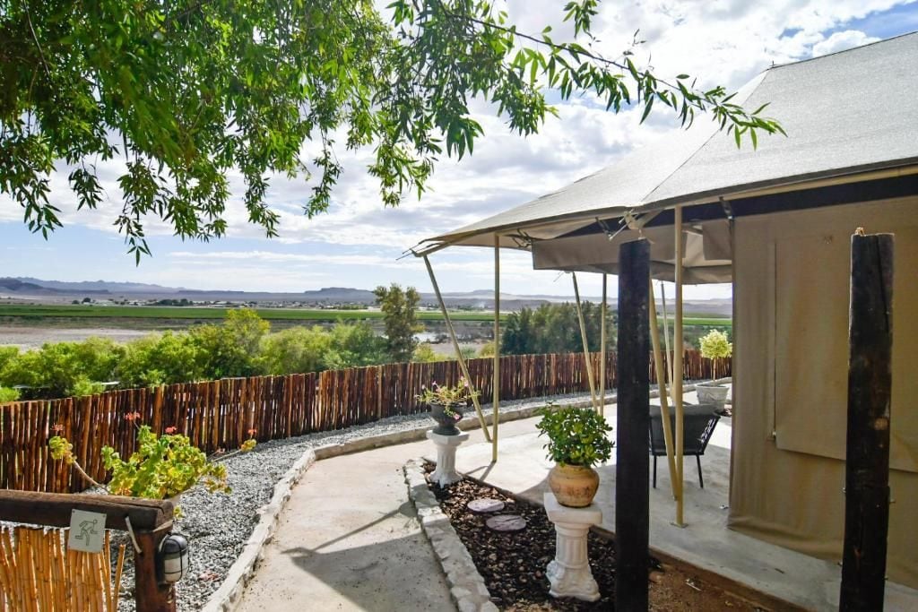 Un patio techado al aire libre con vista a un paisaje rural, cerca hay una valla de madera y plantas en macetas.