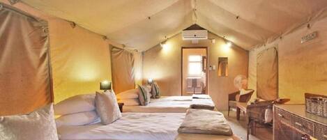 A tented accommodation with two beds, a small table, and a chair.