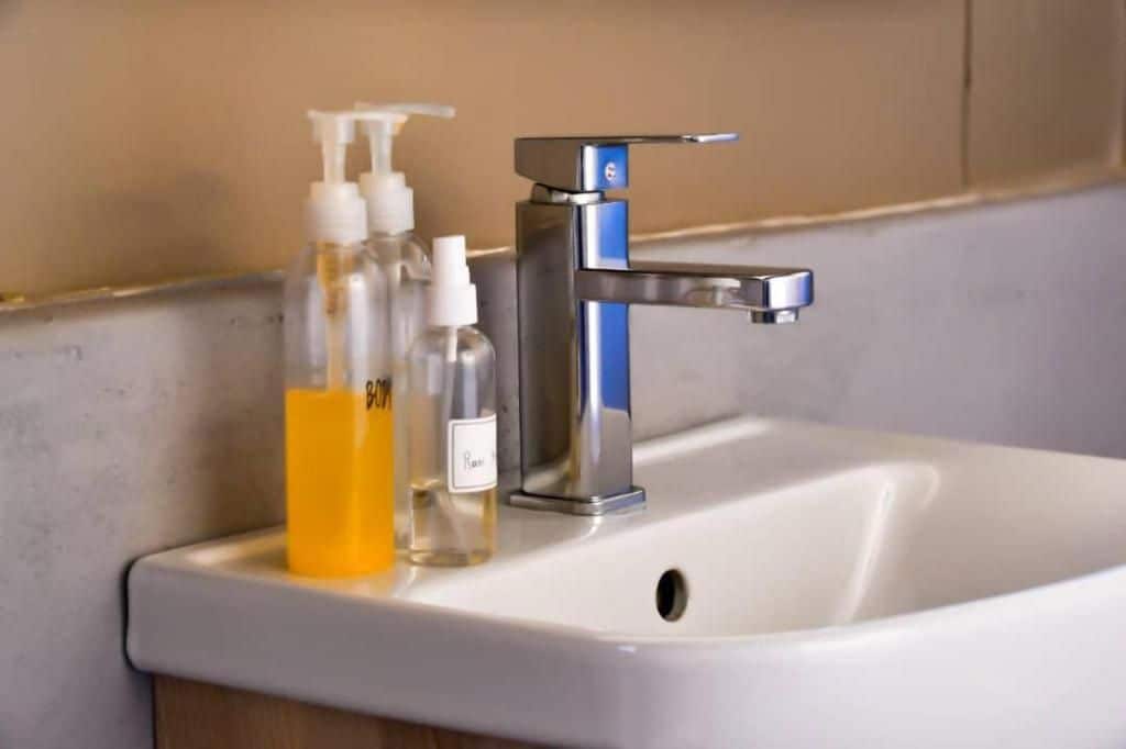 A bathroom sink with a chrome faucet and two bottles of liquid soap.