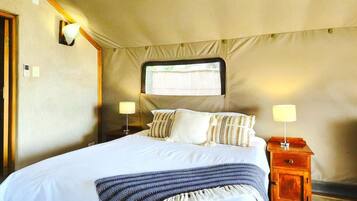 A bed with a headboard, two bedside tables with lamps, and a window with curtains.