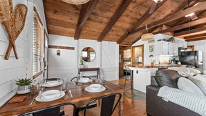 Un interior acogedor con una mesa de madera dispuesta para cuatro comensales, un sofá de cuero y una cocina al fondo.