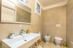 A bathroom with a large sink, mirror, bidet, and toilet. - Resort Beach San Gemiliano (Arbatax)