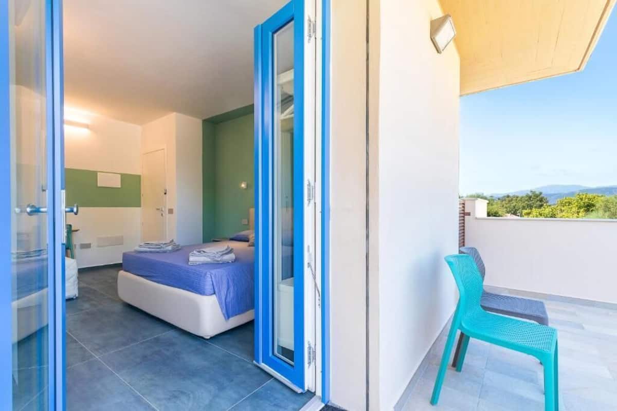 Une chambre à coucher avec un lit, une salle de bain et un balcon équipé d’une chaise.