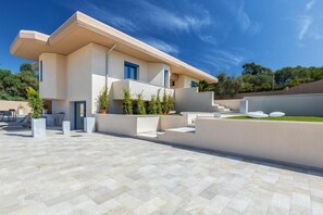 A modern two-story house with a flat roof, a balcony, and a paved courtyard. - Resort Beach San Gemiliano (Arbatax)