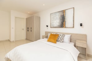 Une chambre à coucher avec un lit, une table de chevet, une lampe fixée au mur et une porte.